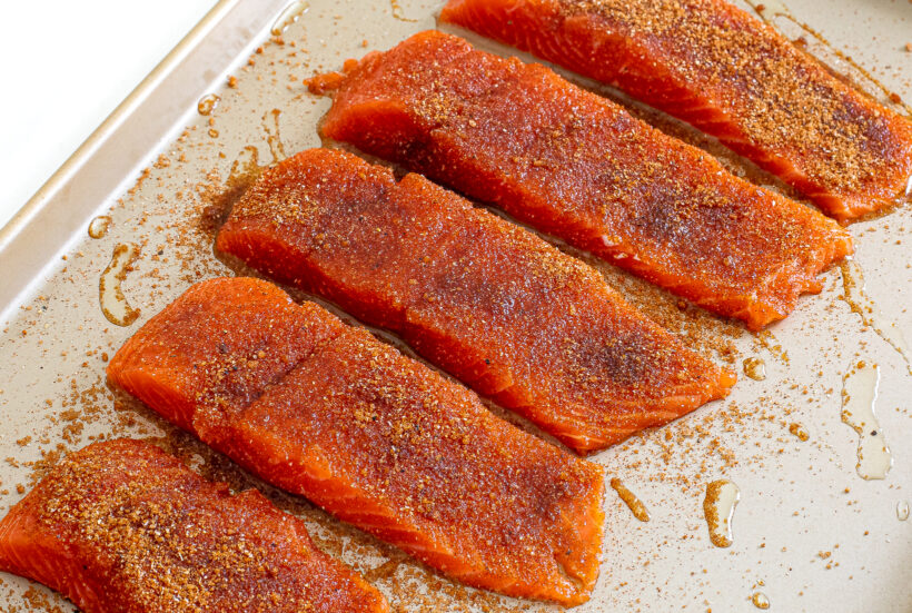 Raw salmon seasoned with a homemade BBQ dry rub on a sheet pan.