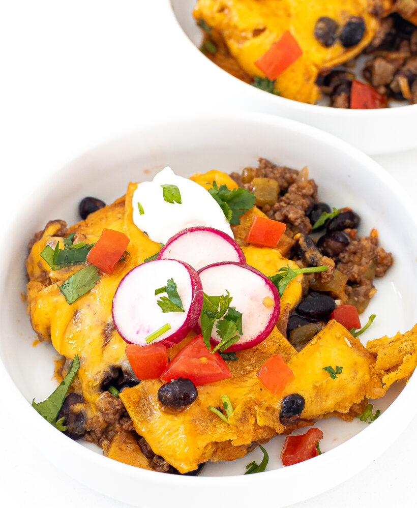 Beef enchilada casserole served in a white bowl topped with sour cream and radishes. 