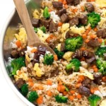 beef fried rice in pan with wooden spoon and veggies