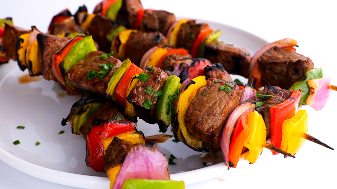 grilled beef kabobs on white plate sprinkled with fresh parsley