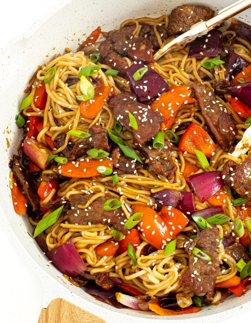 A large skillet with beef lo mein topped with green onions and sesame seeds.