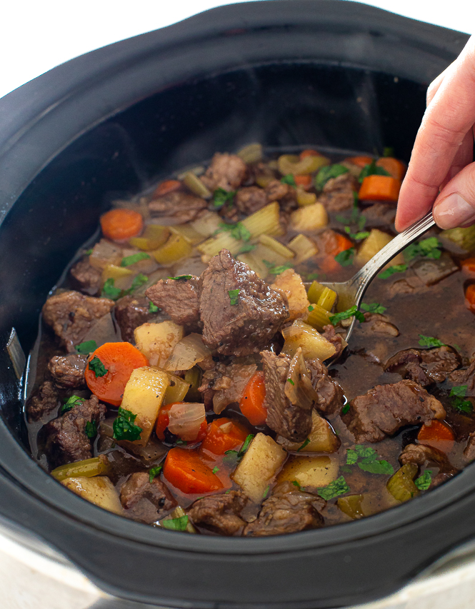 spooning beef stew out of slow cooker