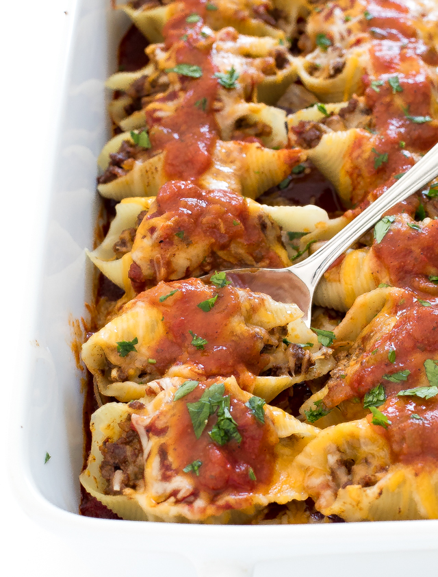 scooping out a stuffed mexican shell from white casserole dish