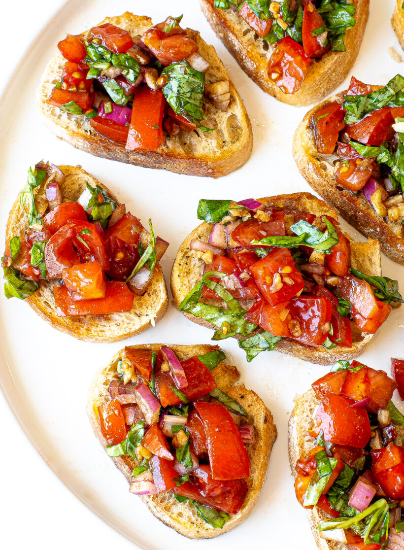Easy Bruschetta Recipe | chefsavvy.com close up shot of a plate of bruschetta with fresh basil on top and tomatoes