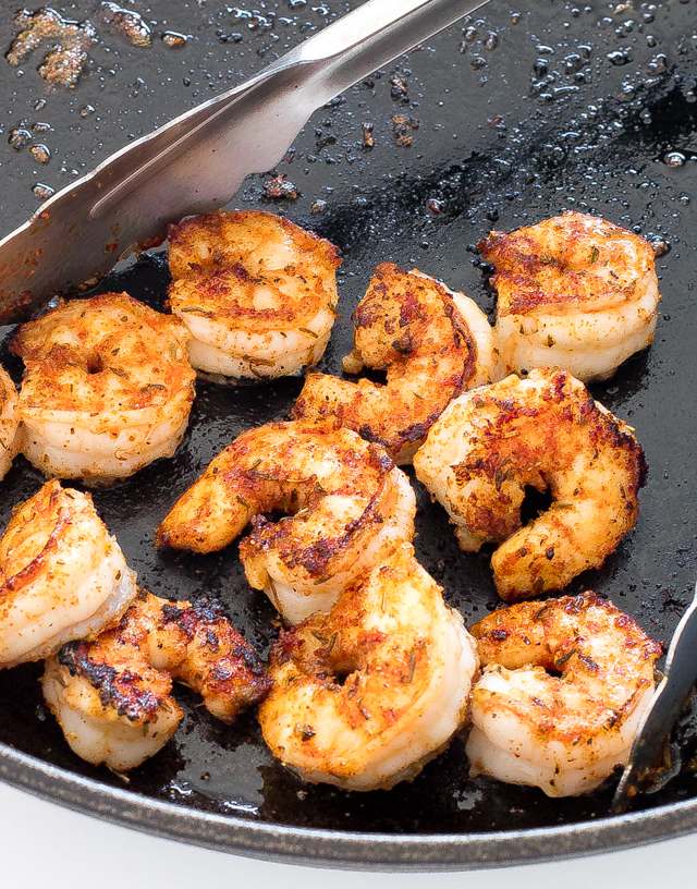 blackened shrimp in cast iron skillet with metal tongs