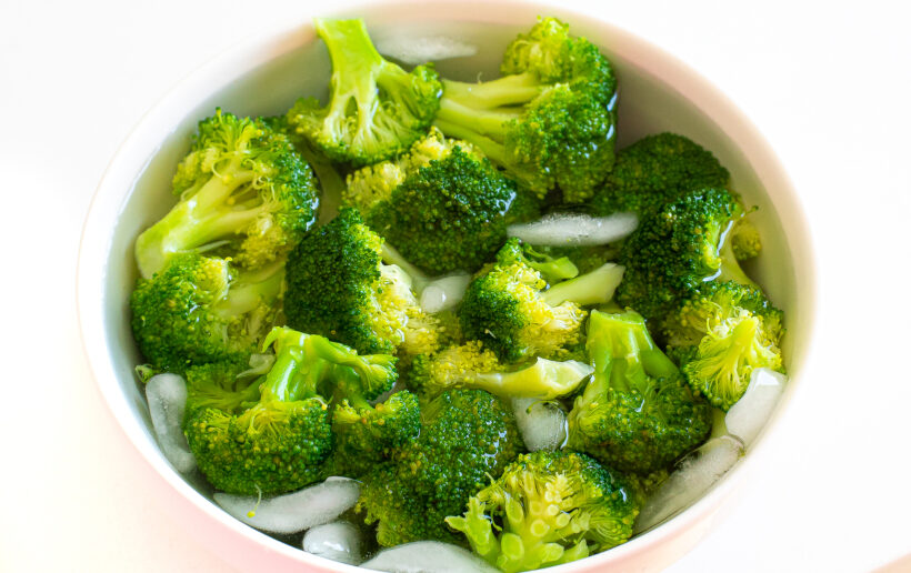 Blanched broccoli in an ice bath in a bowl.