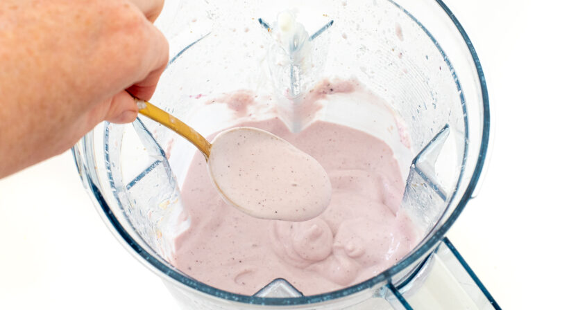 Ingredients in blender after being blending with a hand holding up a spoon to show the texture. 