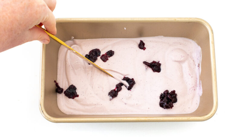 Blueberry ice cream being swirled with extra blueberry jam in a loaf pan. 