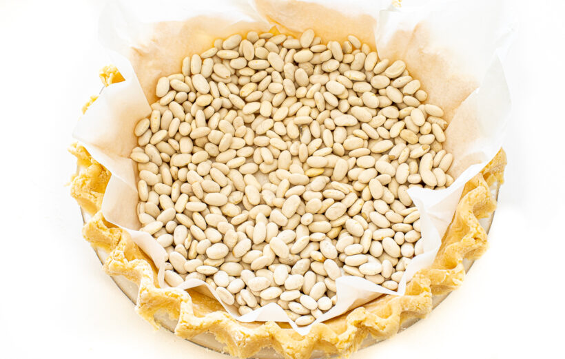 Parchment paper and beans added to pie crust for blind baking.