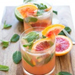 two blood orange mojitos on a wooden cutting board with fresh mint and slices or blood oranges | chefsavvy.com