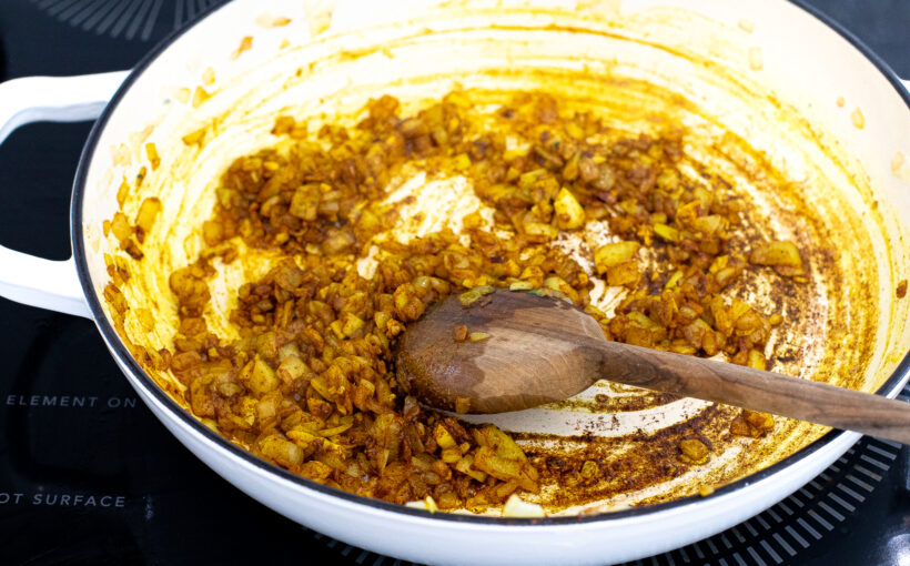 Onions and garlic sautéing with spices in a skillet. 