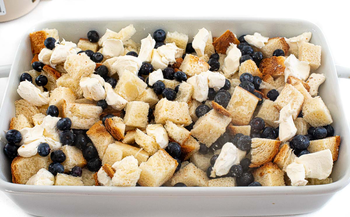 adding cream cheese and blueberries onto unbaked French toast casserole