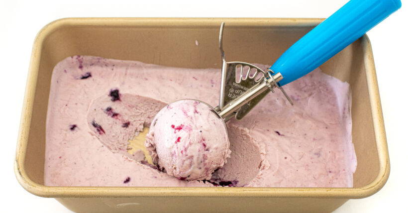 Blueberry ice cream after being frozen with an ice cream scooper scooping a ball. 