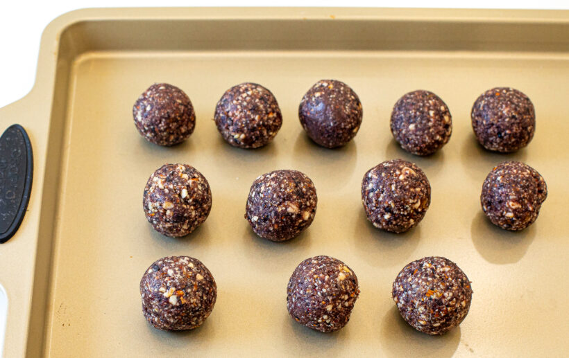 Blueberry energy bites lined up on a baking sheet after being rolled. 
