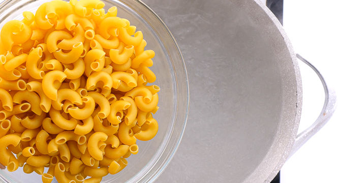 adding elbow macaroni to large pot of boiling water.