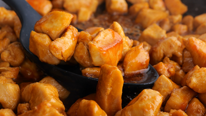 Mixing the chicken and the bourbon sauce with a black spoon.