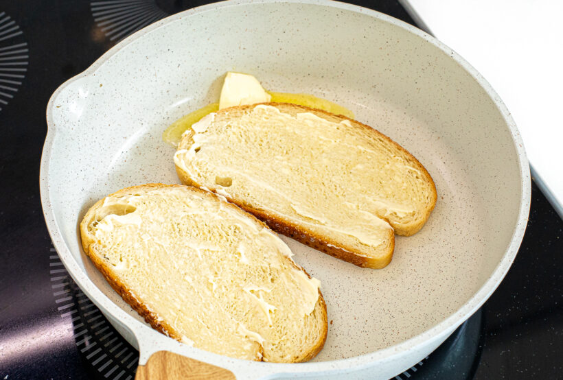 Two slices of bread in a pan spread with mayonnaise on top. 