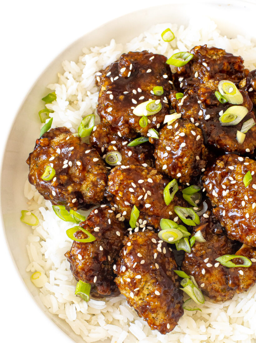 overhead shot of asian chicken bites over white rice with green onions