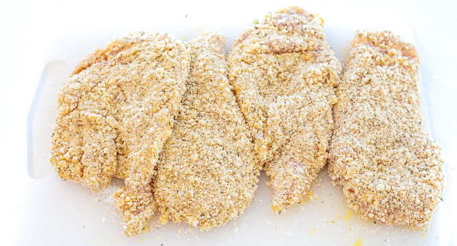 Raw breaded chicken cutlets on a cutting board. 