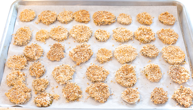 Pickle chips after being dipped in breading, lined up on a baking sheet.