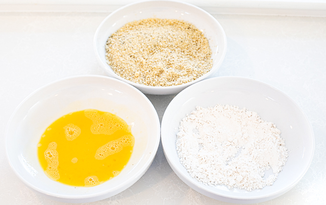 Three bowls, one with egg, one with flour, and one with breadcrumbs. 
