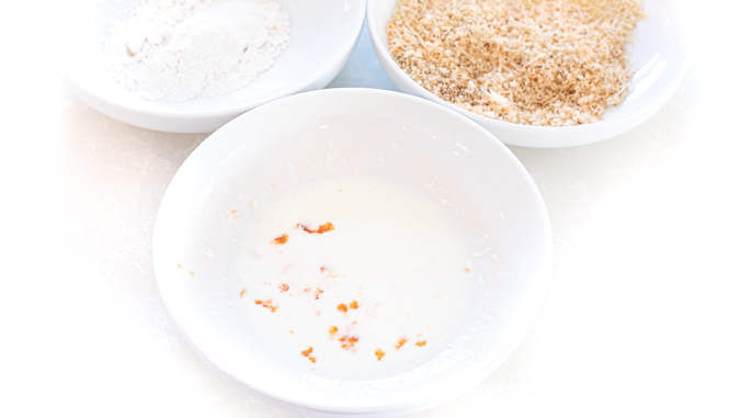 Three white bowls, one with flour, one with buttermilk, and one with breadcrumbs.