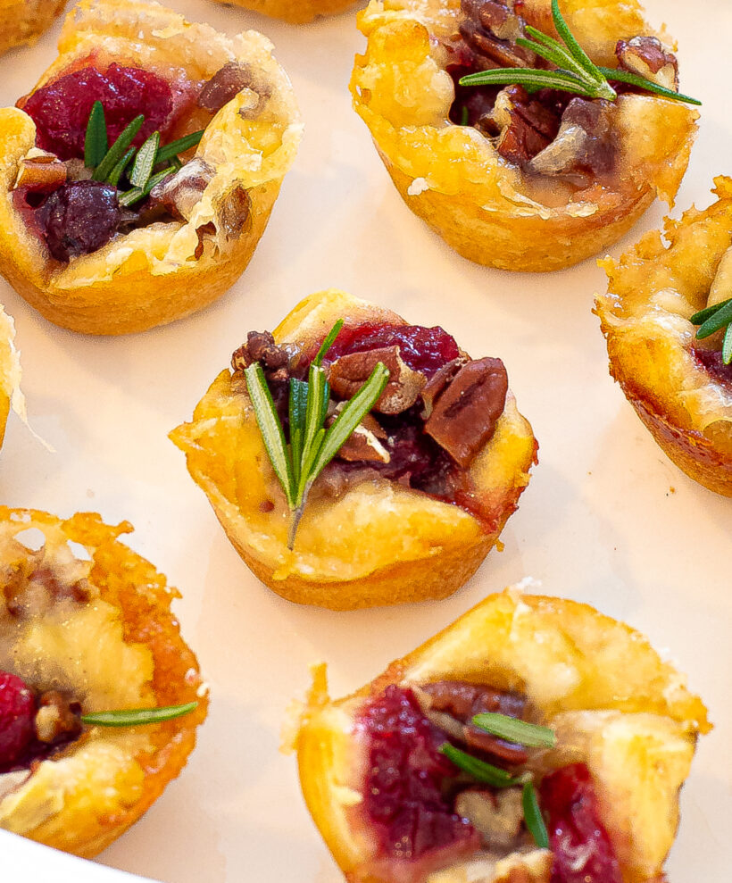Cranberry brie bites on a plate topped with fresh rosemary.