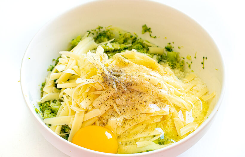 Broccoli in a bowl with shredded cheese, spices and egg.