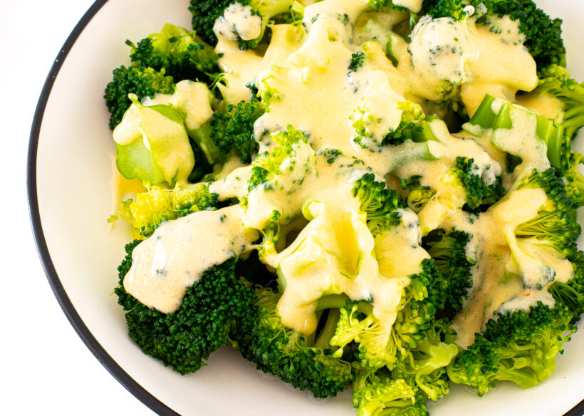 Broccoli topped with cheese sauce in a white and black serving bowl.
