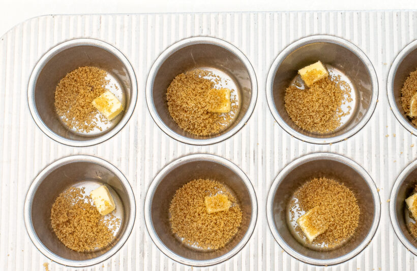 Muffin tin cavities with a small layer of brown sugar and a pieces of butter.