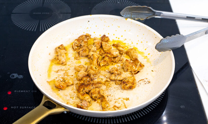 Chicken sautéing in a white skillet.