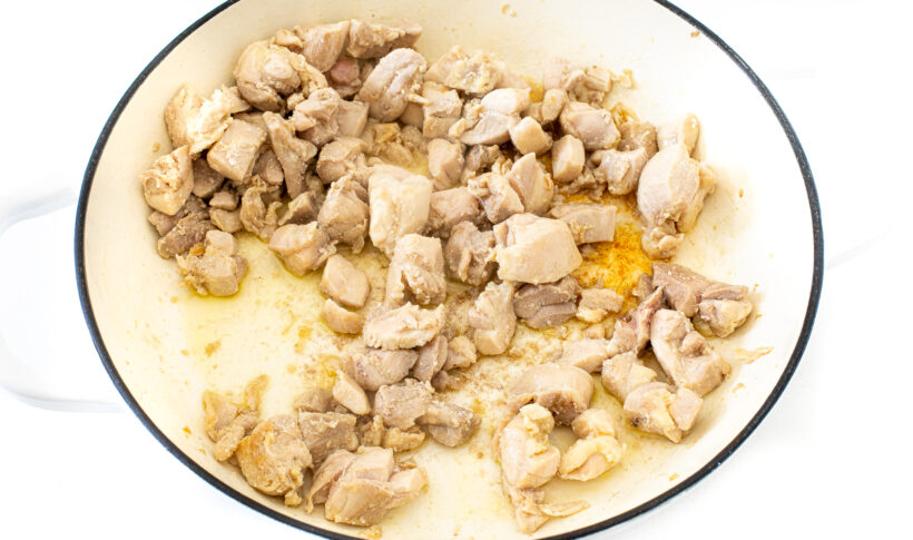 Pieces of chicken in a white skillet.