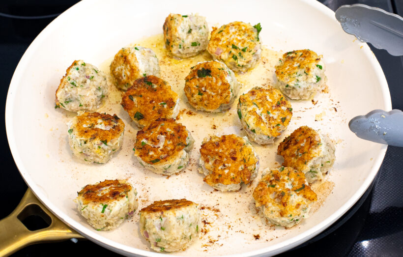 Meatballs being browned in a white skillet.