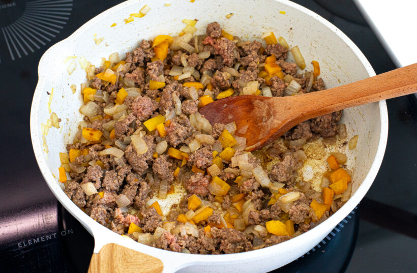 Ground beef being browned with the onion mixture in a skillet. 