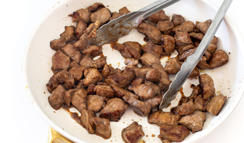Pork being cooked in a white skillet.