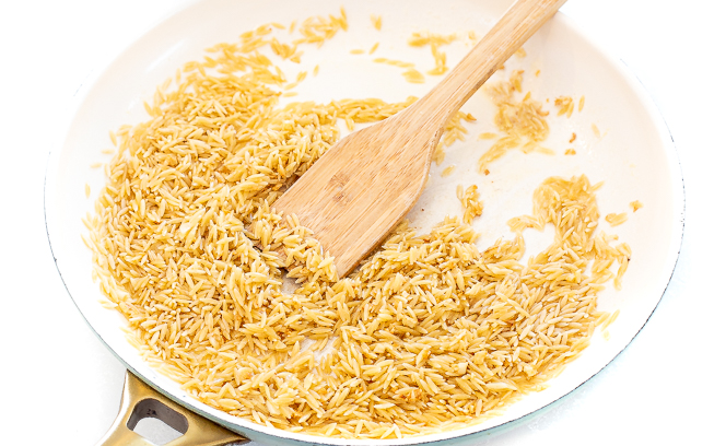 Orzo in a white skillet with a wooden spoon.