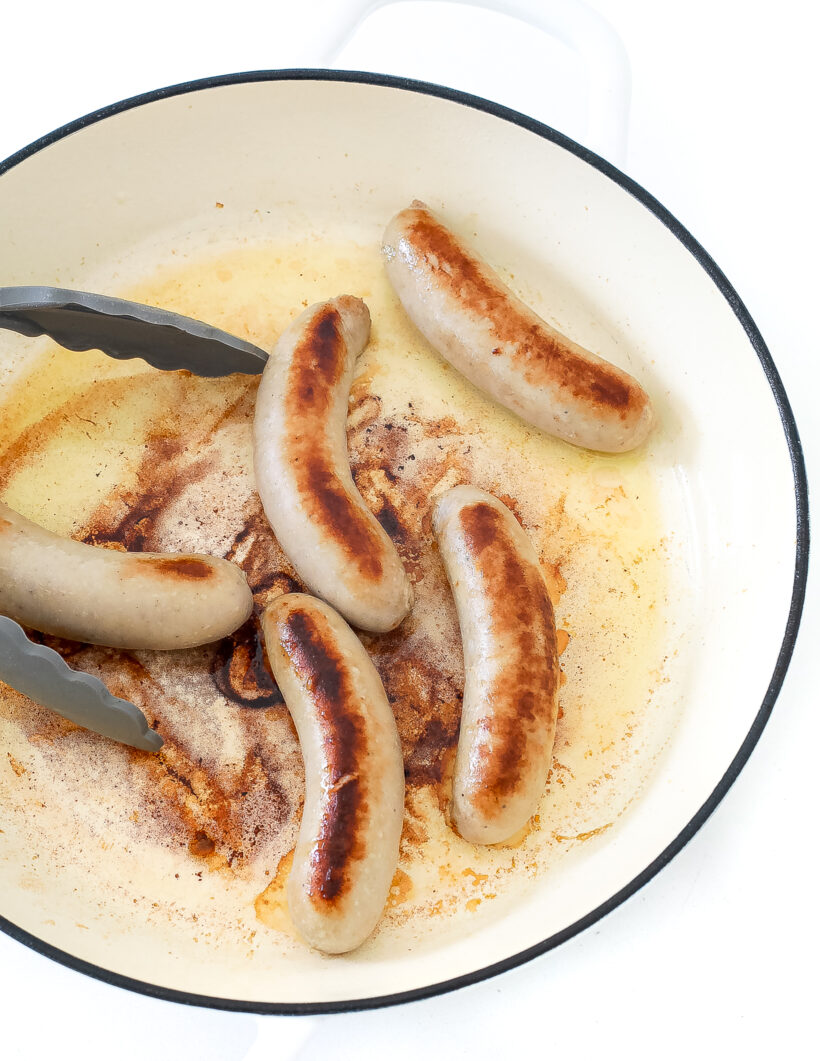Sausages cooking in a skillet.