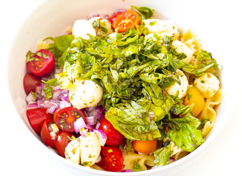 Ingredients for bruschetta pasta salad in a mixing bowl before being mixed. 