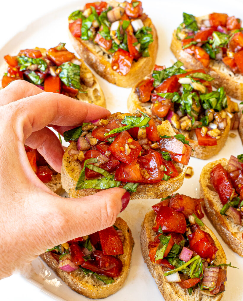 Bruschetta | chefsavvy.com author holding a piece of toasted baguette with bruschetta on top