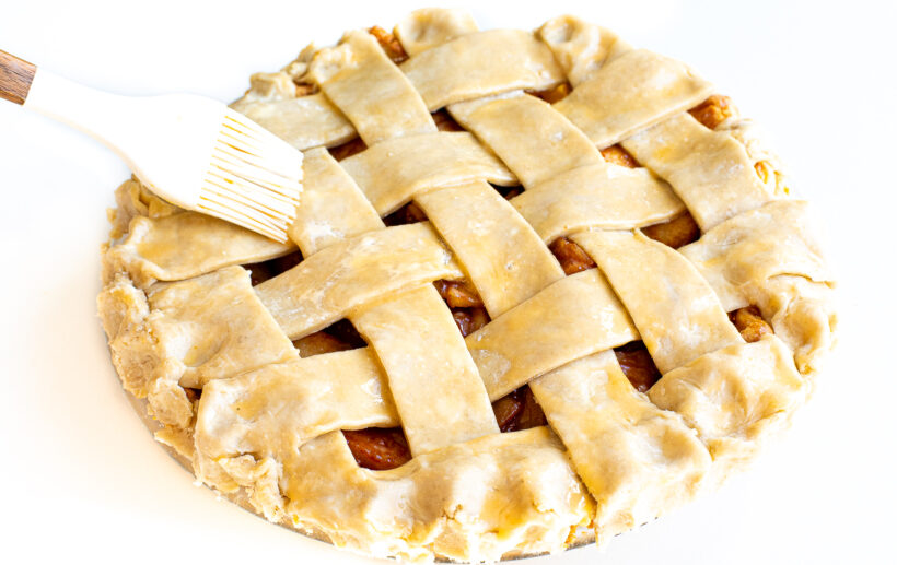 Pastry brush brushing lattice top pie crust with egg wash.