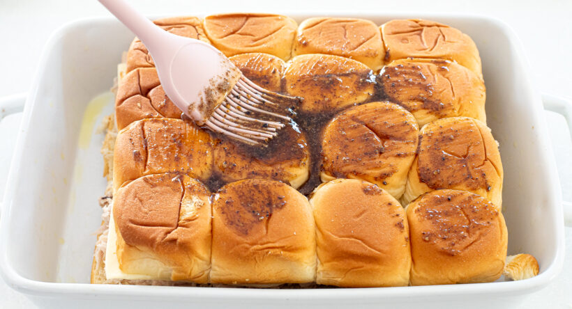 Brown butter glaze being brushed on top of the assembled sliders.