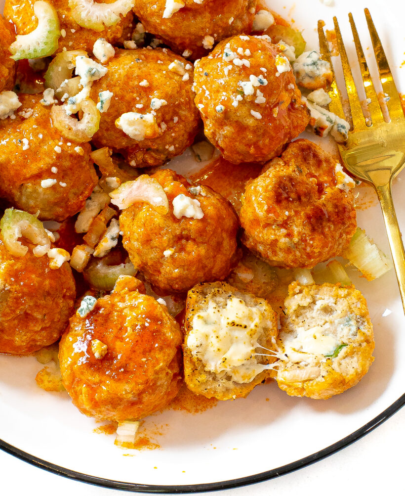 A close up photo of blue cheese meatballs topped with chopped celery and blue cheese crumbles on a white plate.