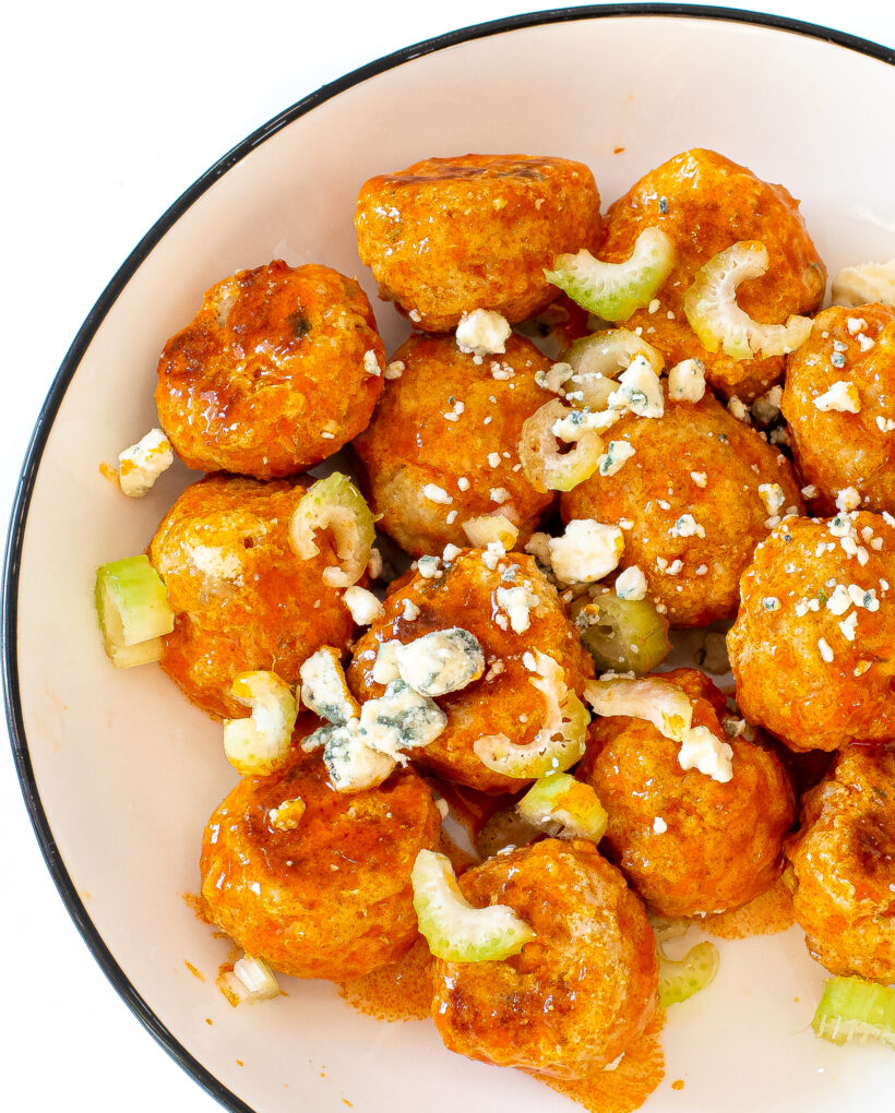 A top down view of buffalo meatballs topped with celery and blue cheese crumbles in a white serving bowl.