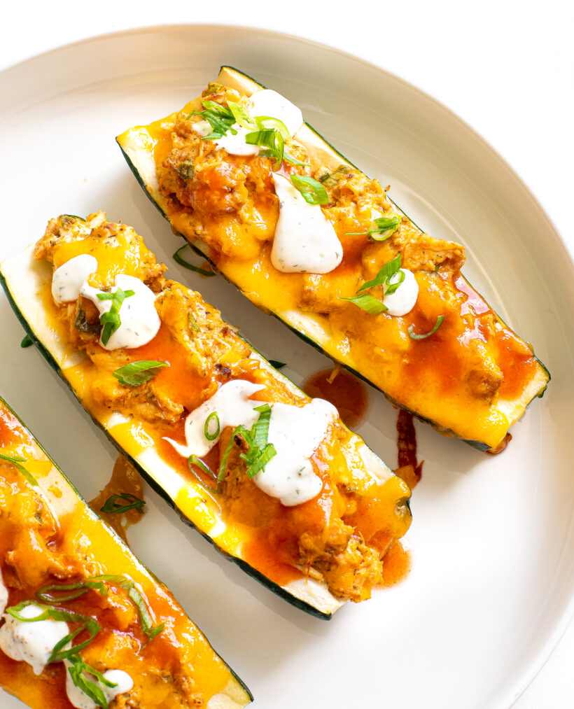 Buffalo chicken zucchini boats served on a plate with ranch and buffalo sauce drizzled on top.