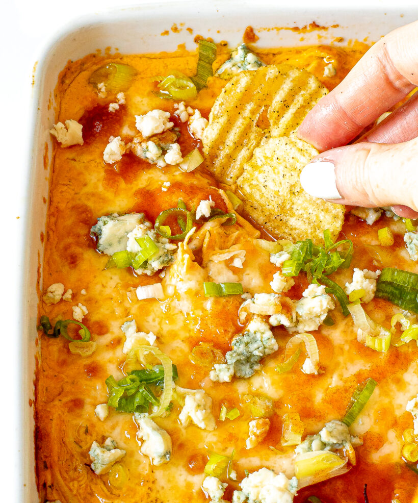 Hand dipping potato chip into buffalo chicken dip.