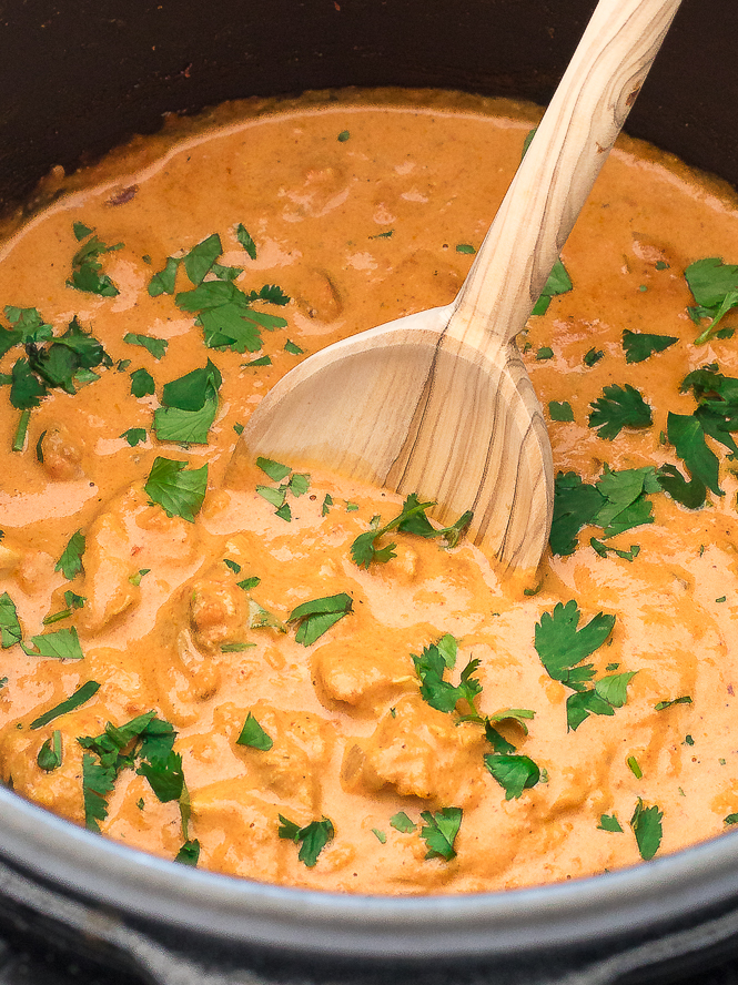 butter chicken in slow cooker with wooden spoon