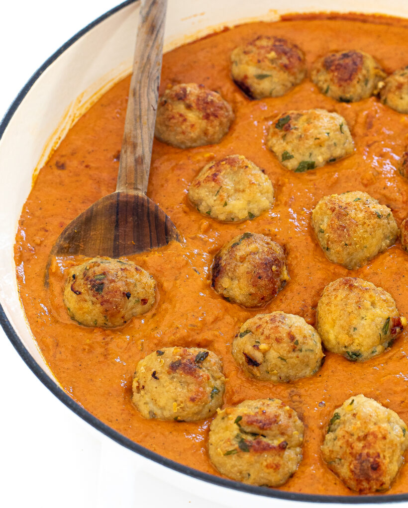 Chicken meatballs in a butter curry sauce in a skillet with a wooden spoon. 