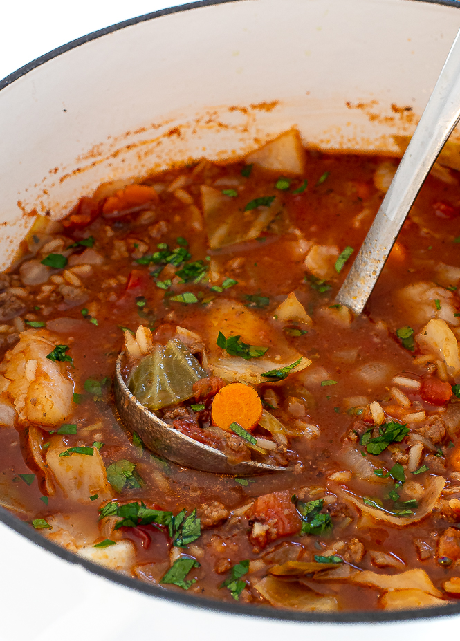 Close up of cabbage roll soup in a pot with a silver ladle.