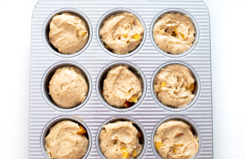 cake batter and peaches in muffin tin