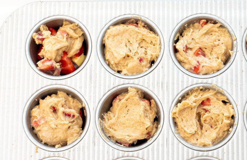 Muffin tin with strawberry cake batter inside of each cavity before baking. 